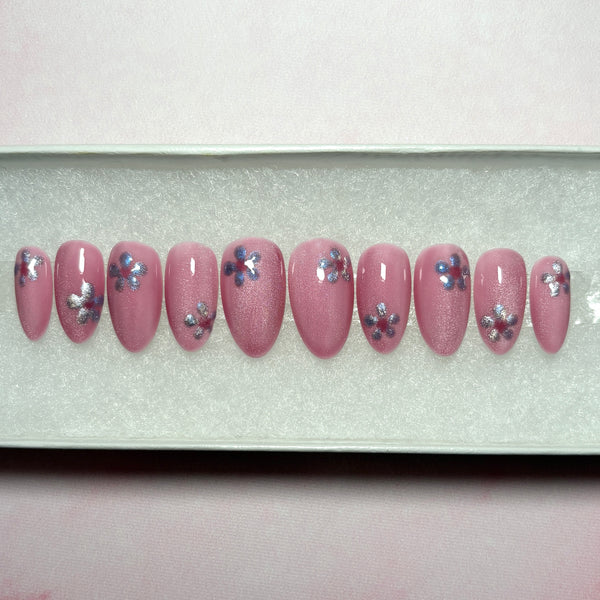 Load image into Gallery viewer, Pink handmade press-on nails in a short almond shape, in cat eye shimmery blush pink, with a lilac-silver cat-eye flower on each nail, displayed in a white presentation box.
