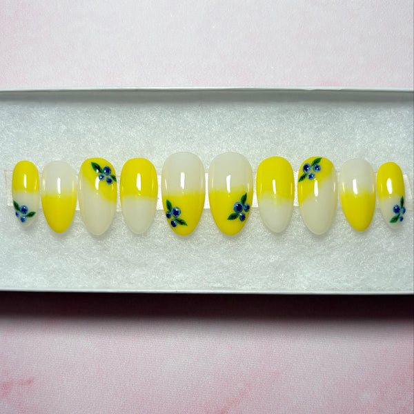 Load image into Gallery viewer, Short almond handmade press-on nails in a bright yellow ombre embellished with delicate 3D blueberries, displayed in a white presentation box.
