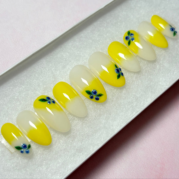 Load image into Gallery viewer, Handmade false nails featuring delicate 3D blueberries designed on a lemon-yellow ombre base, in a short almond shape, in a white presentation box.

