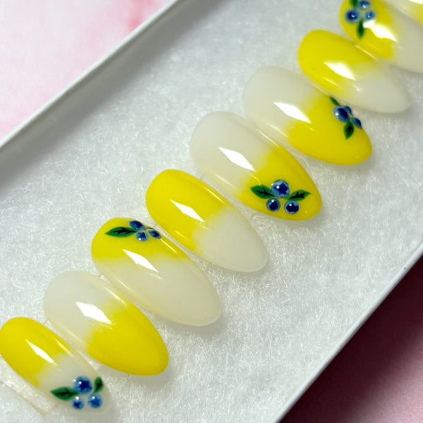 Load image into Gallery viewer, Yellow and milky-white ombre press-on nails with delicate 3D blueberries design, in a short almond shape, displayed in a white presentation box.
