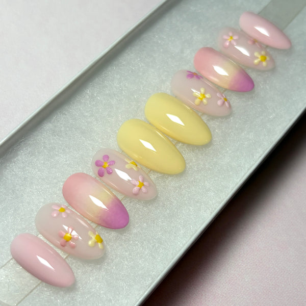 Load image into Gallery viewer, Almond-shaped floral press-on nails in soft pastel yellows and pinks with delicate pastel flowers in pinks and whites and an ombre design, in a white presentation box. 
