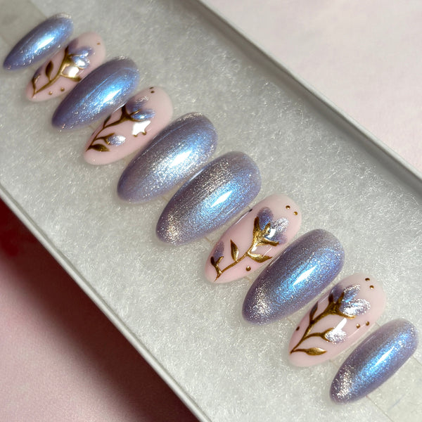 Load image into Gallery viewer, Short almond press-on nails in shimmering lilac-silver cat eye and soft pink featuring delicate flowers with gold chrome stems and leaves, and shimmering lilac petals on a pastel pink base from Illuminate by Liana.
